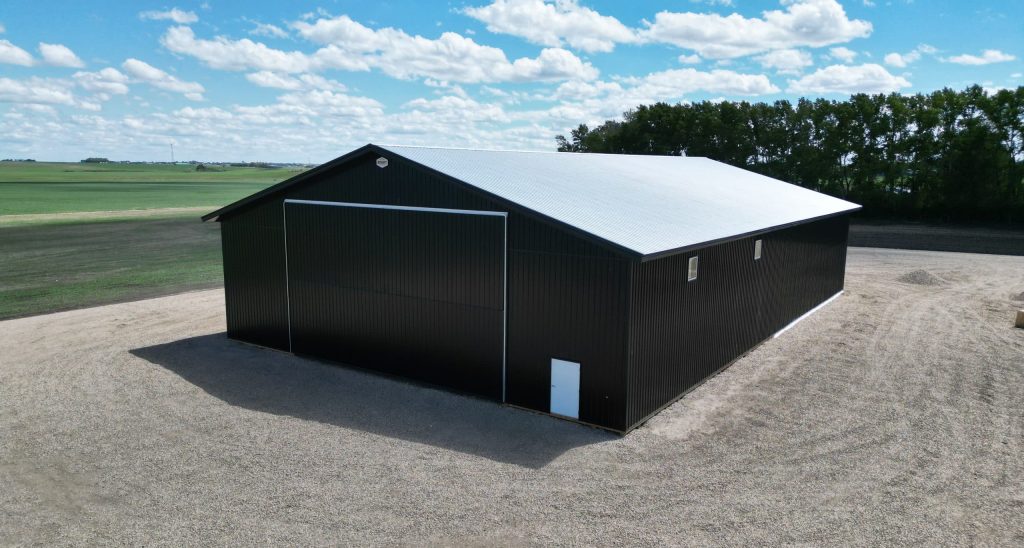 A black post-frame machine shed with a black bi-fold door and two overhead doors