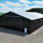 A black post-frame machine shed with a black bi-fold door and two overhead doors