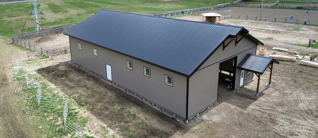 A buckskin post-frame equestrian barn with timber accents, soffits, and a overhead door