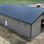 A buckskin post-frame equestrian barn with timber accents, soffits, and a overhead door
