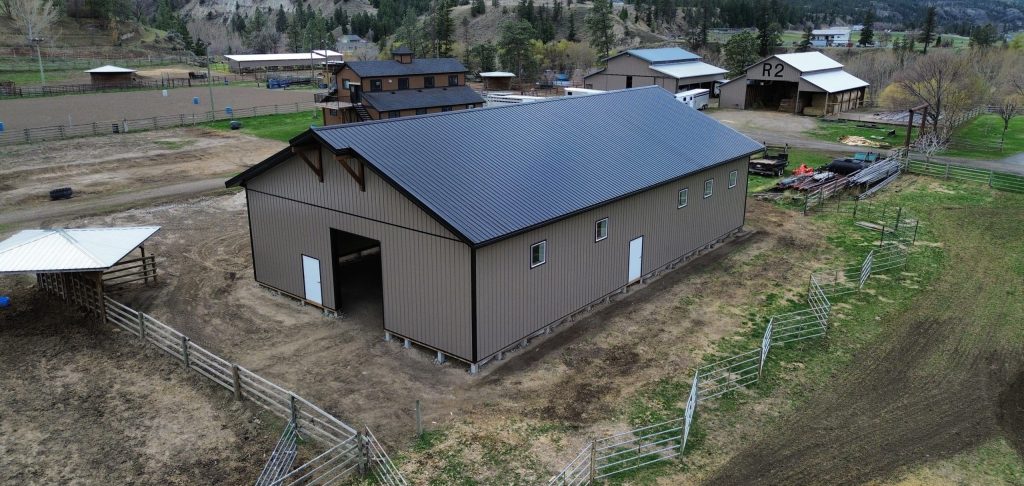 A buckskin post-frame equestrian barn with timber accents, soffits, and a overhead door