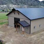A buckskin post-frame equestrian barn with timber accents, soffits, and a overhead door