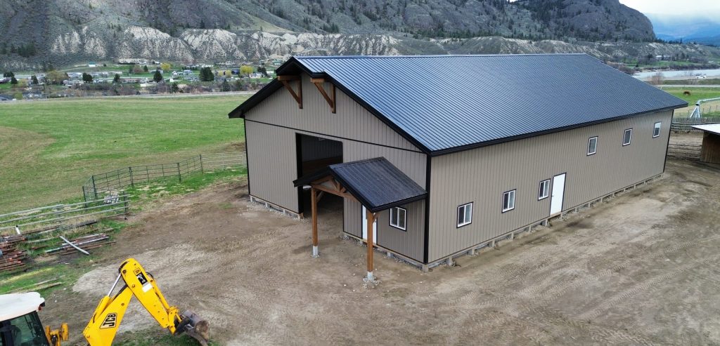 A buckskin post-frame equestrian barn with timber accents, soffits, and a overhead door
