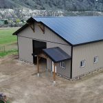 A buckskin post-frame equestrian barn with timber accents, soffits, and a overhead door