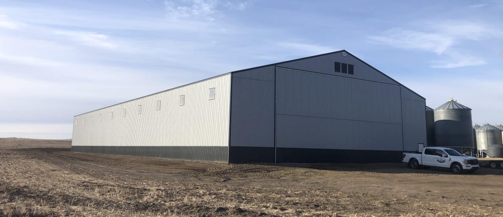 A ascot grey post-frame agricultural storage building with two bi-fold doors and wainscoting
