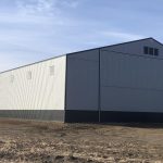 A ascot grey post-frame agricultural storage building with two bi-fold doors and wainscoting