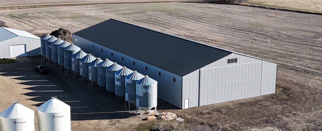 A ascot grey post-frame agricultural storage building with two bi-fold doors and wainscoting