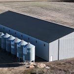 A ascot grey post-frame agricultural storage building with two bi-fold doors and wainscoting