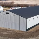 A ascot grey post-frame agricultural storage building with two bi-fold doors and wainscoting