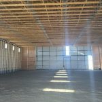 A ascot grey post-frame agricultural storage building with two bi-fold doors and wainscoting
