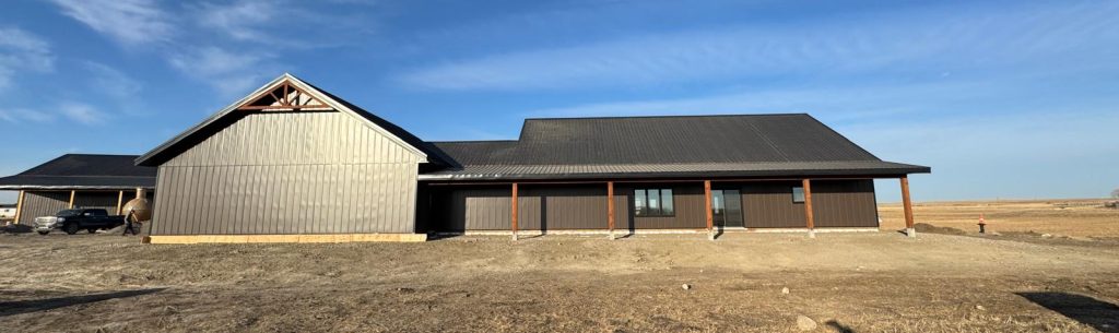 A coffee brown post-frame barndominium with three overhead doors, timber accents, soffits, and open and closed lean-tos