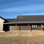 A coffee brown post-frame barndominium with three overhead doors, timber accents, soffits, and open and closed lean-tos