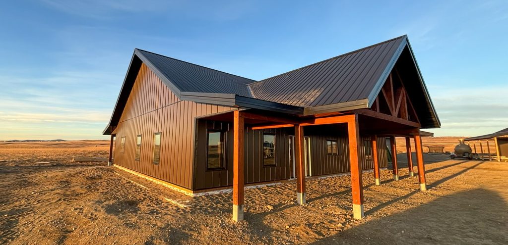 A coffee brown post-frame barndominium with three overhead doors, timber accents, soffits, and open and closed lean-tos