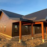 A coffee brown post-frame barndominium with three overhead doors, timber accents, soffits, and open and closed lean-tos