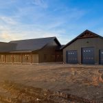 A coffee brown post-frame barndominium with three overhead doors, timber accents, soffits, and open and closed lean-tos