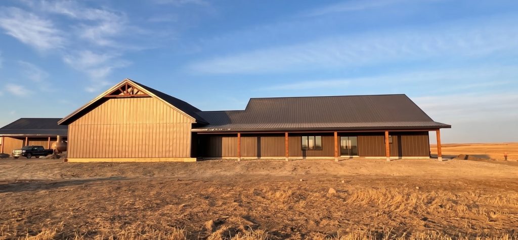 A coffee brown post-frame barndominium with three overhead doors, timber accents, soffits, and open and closed lean-tos
