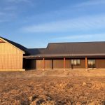 A coffee brown post-frame barndominium with three overhead doors, timber accents, soffits, and open and closed lean-tos