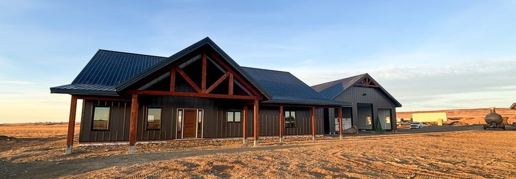 A coffee brown post-frame barndominium with three overhead doors, timber accents, soffits, and open and closed lean-tos