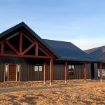 A coffee brown post-frame barndominium with three overhead doors, timber accents, soffits, and open and closed lean-tos