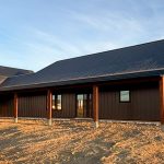 A coffee brown post-frame barndominium with three overhead doors, timber accents, soffits, and open and closed lean-tos