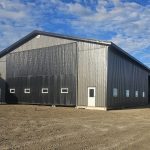 A charcoal post-frame agricultural shop with a closed lean-to, a bi-fold and overhead door