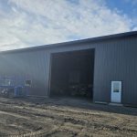 A charcoal post-frame agricultural shop with a closed lean-to, a bi-fold and overhead door