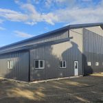 A charcoal post-frame agricultural shop with a closed lean-to, a bi-fold and overhead door