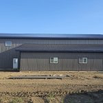 A charcoal post-frame agricultural shop with a closed lean-to, a bi-fold and overhead door