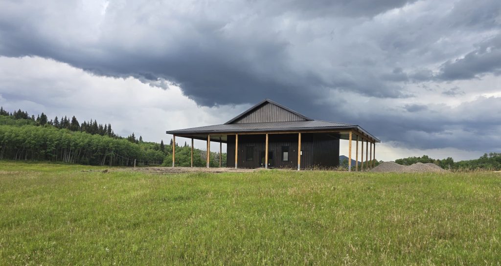 A coffee brown post-frame agricultural shop with wrap around open lean-to and overhead doors