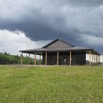 A coffee brown post-frame agricultural shop with wrap around open lean-to and overhead doors