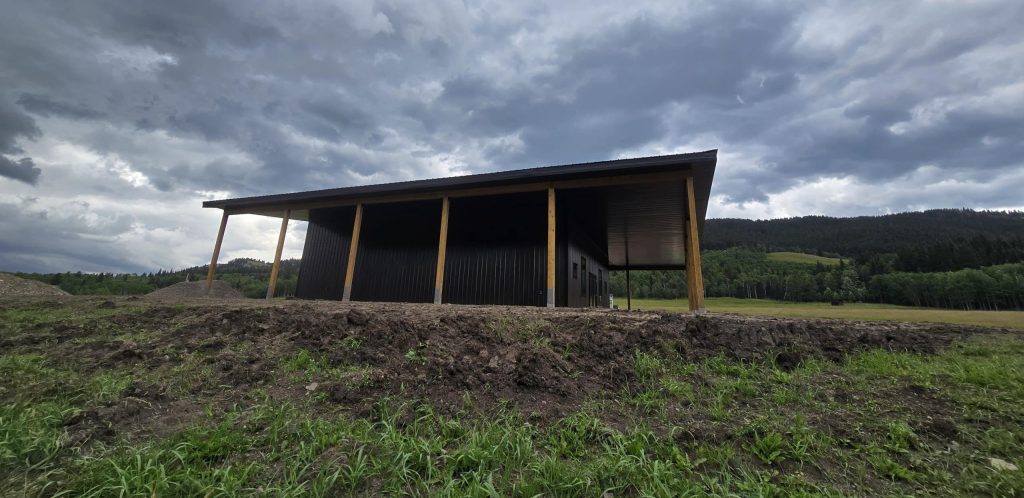 A coffee brown post-frame agricultural shop with wrap around open lean-to and overhead doors