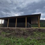A coffee brown post-frame agricultural shop with wrap around open lean-to and overhead doors