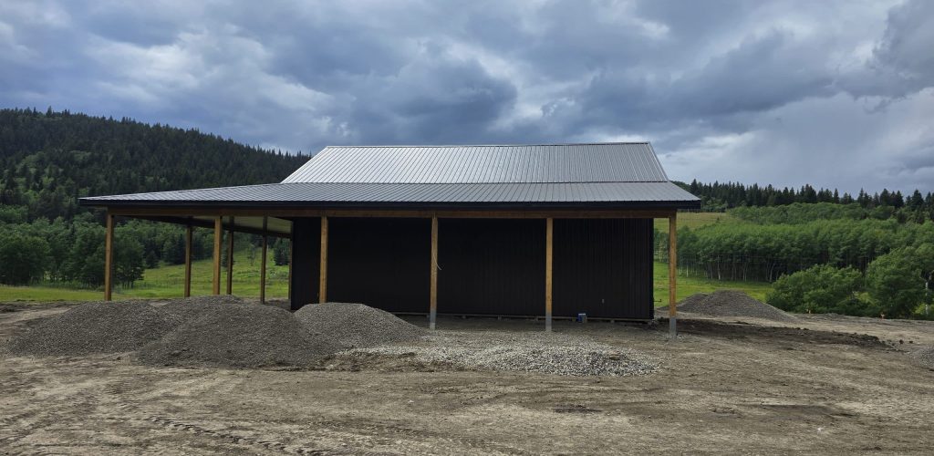 A coffee brown post-frame agricultural shop with wrap around open lean-to and overhead doors