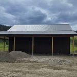A coffee brown post-frame agricultural shop with wrap around open lean-to and overhead doors