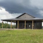 A coffee brown post-frame agricultural shop with wrap around open lean-to and overhead doors