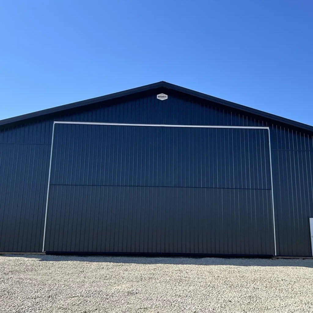 A black post-frame machine shed with a black bi-fold door and two overhead doors