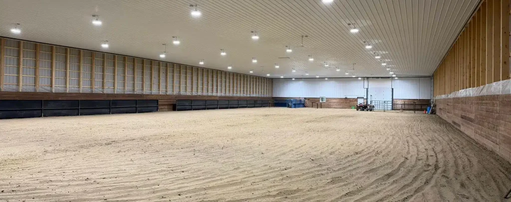 A bright red post-frame equestrian barn with overhead doors and a black roof