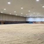A bright red post-frame equestrian barn with overhead doors and a black roof