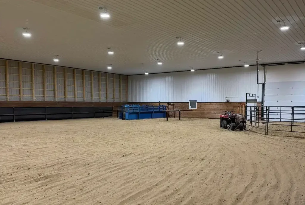 A bright red post-frame equestrian barn with overhead doors and a black roof