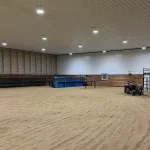 A bright red post-frame equestrian barn with overhead doors and a black roof