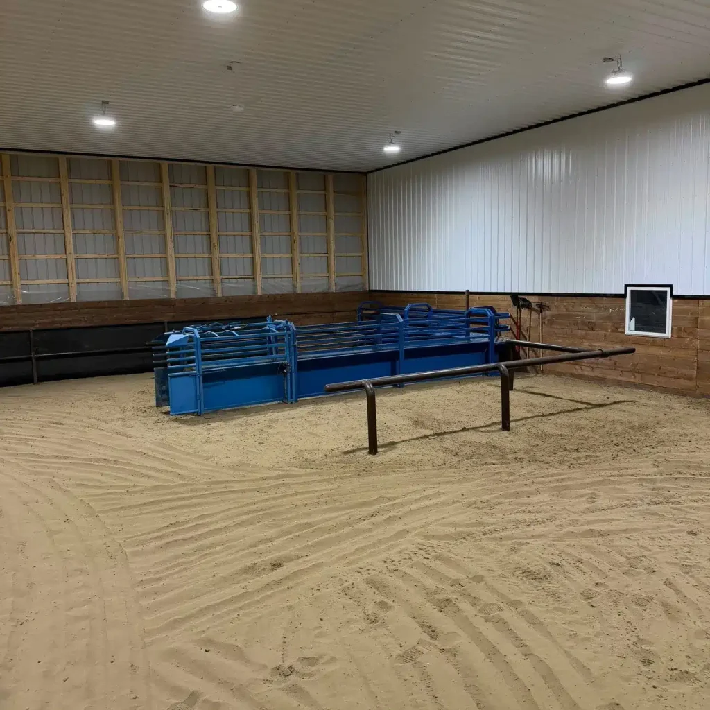 A bright red post-frame equestrian barn with overhead doors and a black roof