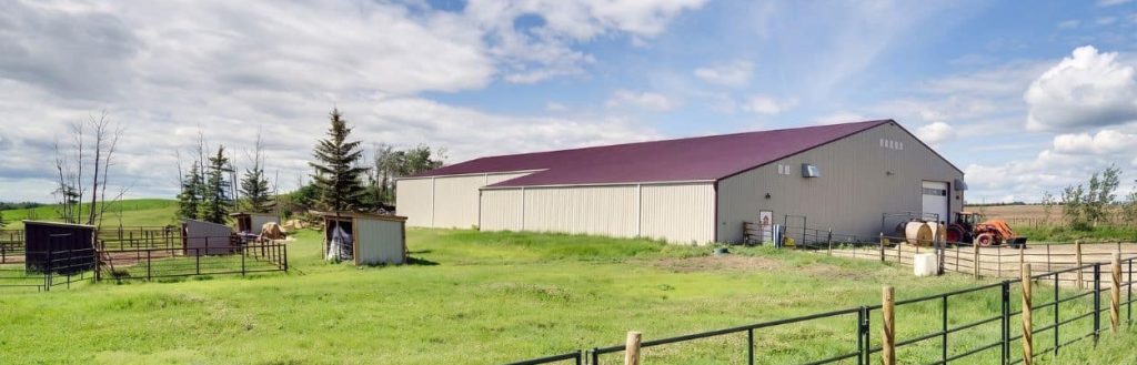 A stone grey post frame equestrian riding arena with attached barn