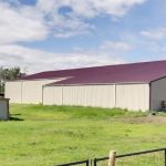 A stone grey post frame equestrian riding arena with attached barn