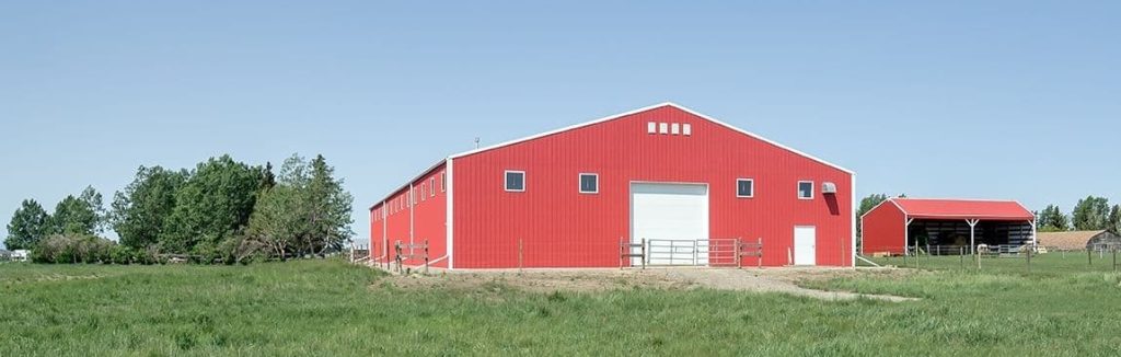 A bright red post-frame riding arena with overhead doors