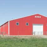 A bright red post-frame riding arena with overhead doors