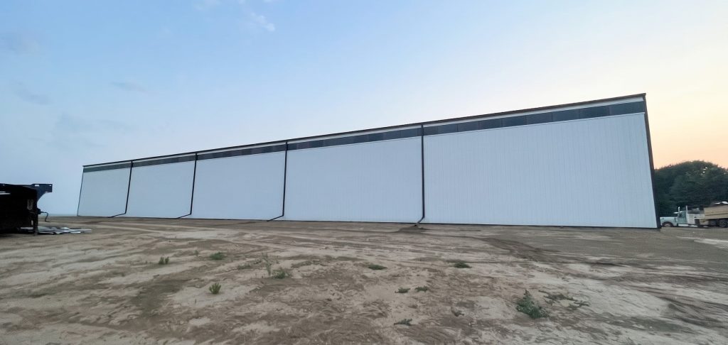 A bright white post-frame agricultural storage building with bi-fold and overhead doors