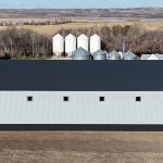 A ascot grey post-frame agricultural storage building with two bi-fold doors and wainscoting