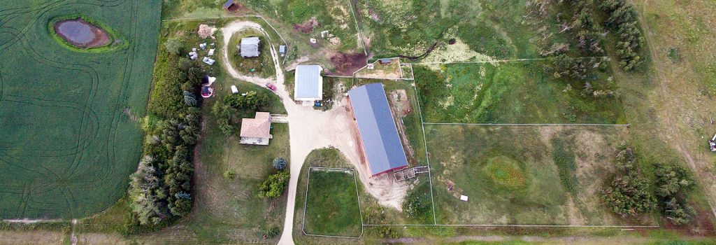A dark red post-frame riding arena with a chain overhead door
