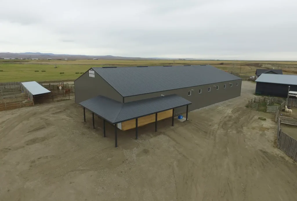 A sable post-frame riding arena with overhead doors, an open lean-to and kickwall