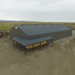 A sable post-frame riding arena with overhead doors, an open lean-to and kickwall